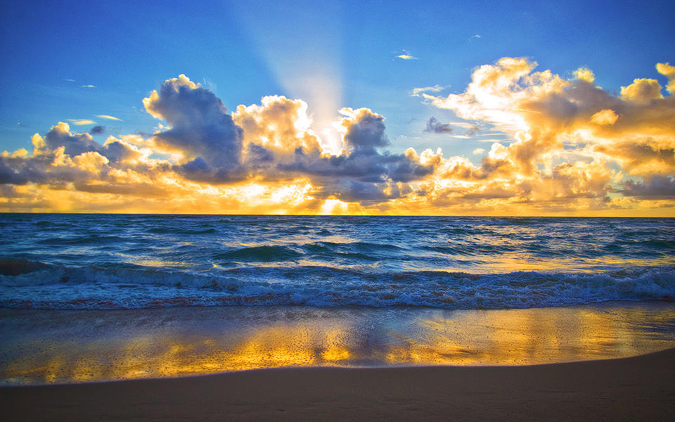 view from a beach of a bright yellow sunrise creaking through the clouds