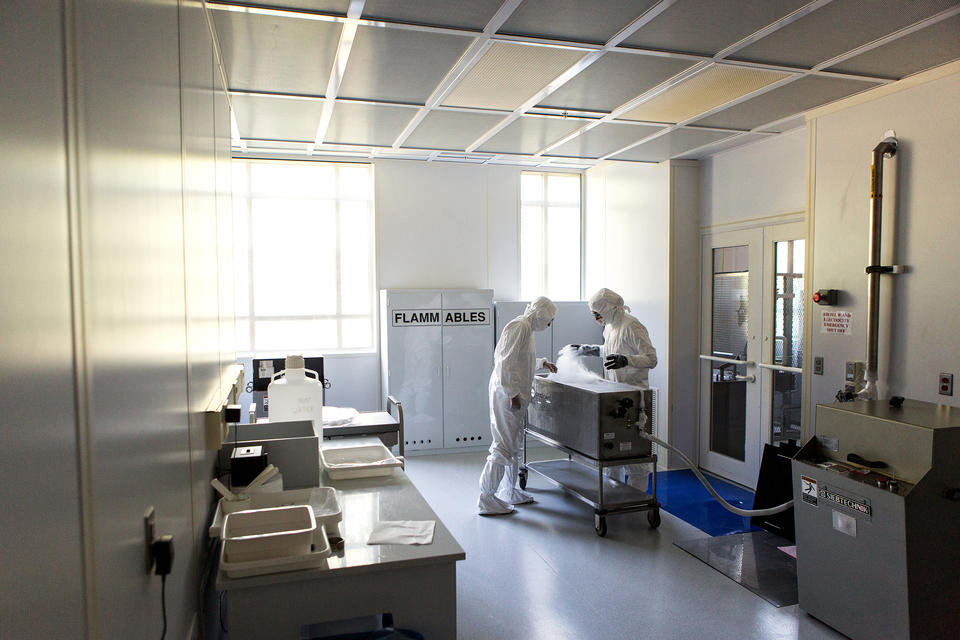 Two scientists wearing hooded suits, gloves and safety goggles work together to prepare samples for long term storage.