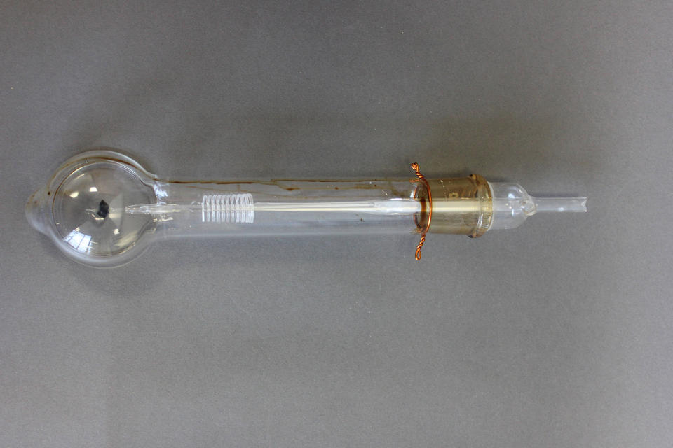 a glass tube with a bulb at one end. there is a glass filament running through the center of the tube that coils on the bulbous end. there is a brass-colored plug at the other end where the tube tapers to a smaller straight tube