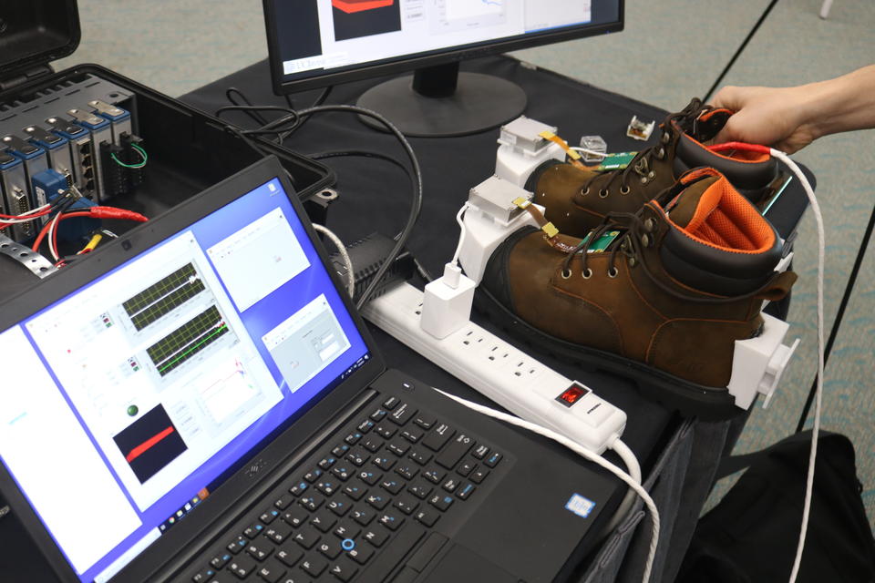A pair of work boots with location tracking technology built in sitting next to a computer monitor