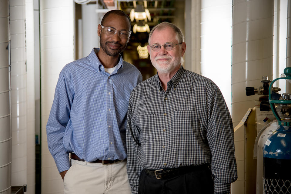 Two men (Bob Vocke and Savelas Rabb) stand in a hallway outside of a lab. They are both smiling