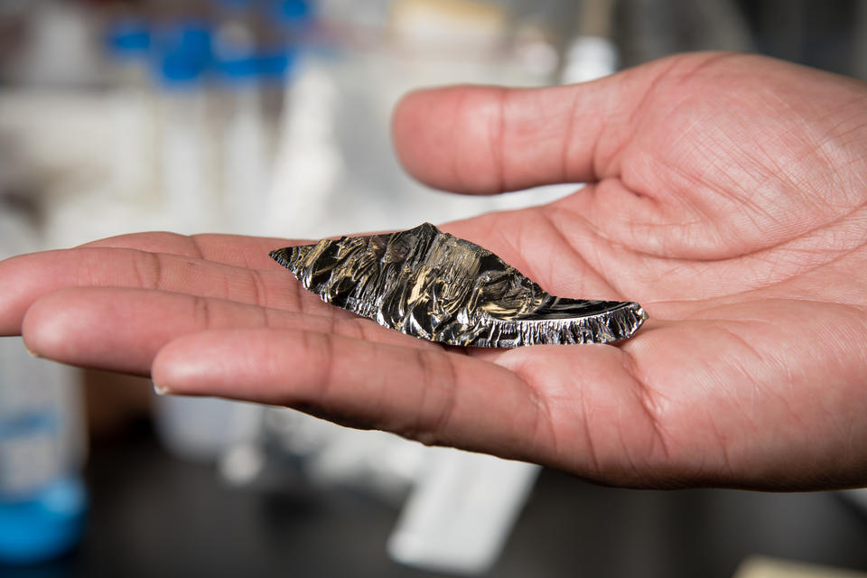 A piece of shiny metalloid with jagged edges is presented in the palm of a man’s hand.