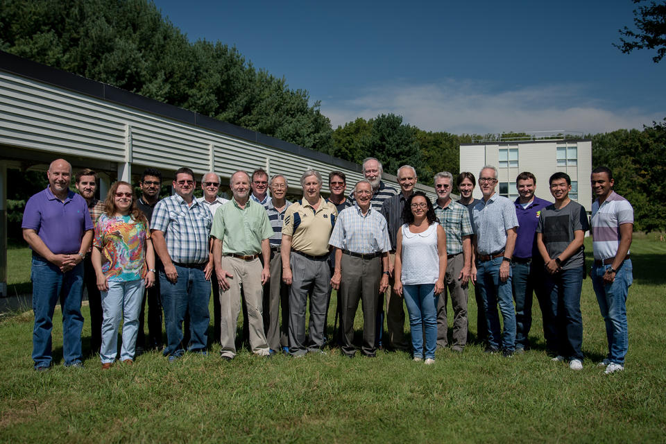 Group of researchers standing in a field in front of a small lab