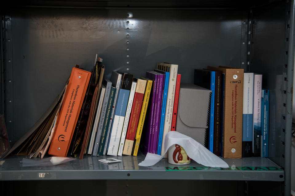 a shelf with books, folders and a small white ceramic mug with a monkey on it