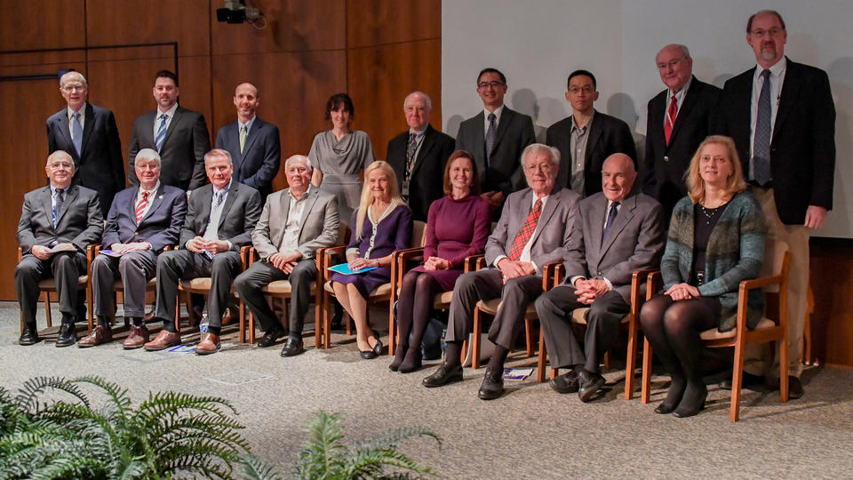 6 men and 3 womens seating with 8 men and 1 woman standing behind them