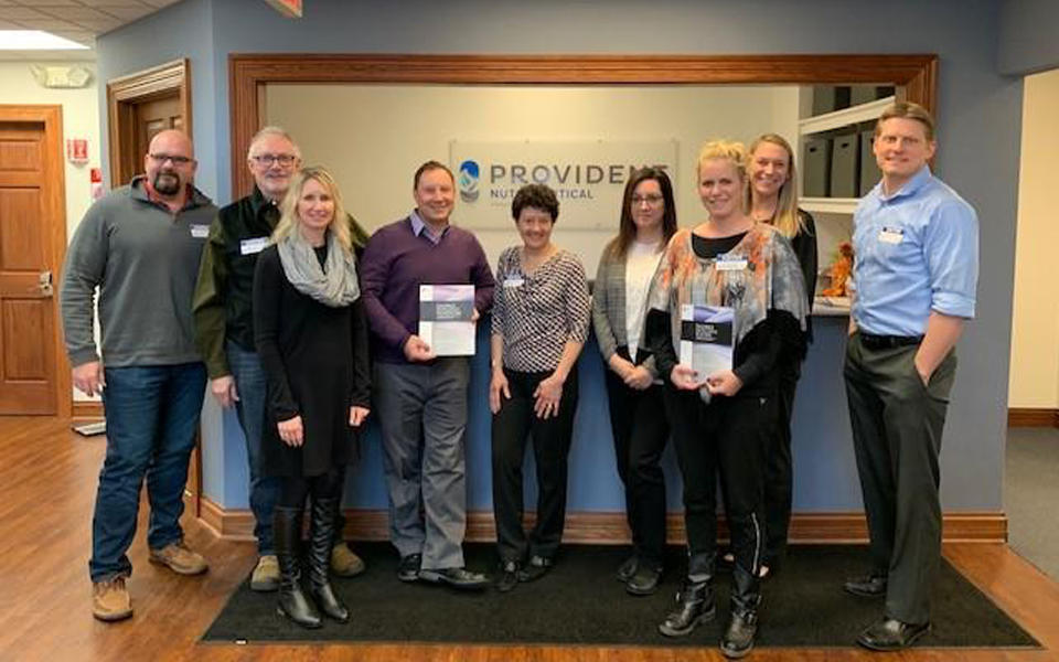 Baldrige Examiner Dawn Garcia with a group of coworkers in Wisconsin holding Baldrige framework booklet.