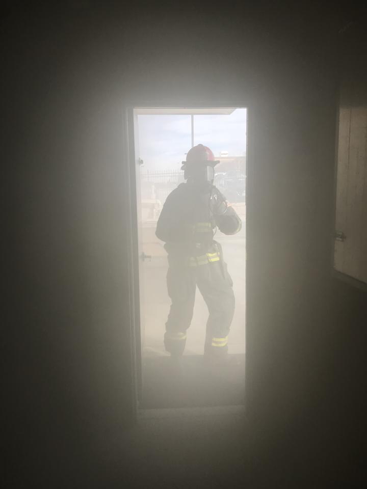Firefighter standing outside in doorway is almost completely obscured by smoke. 