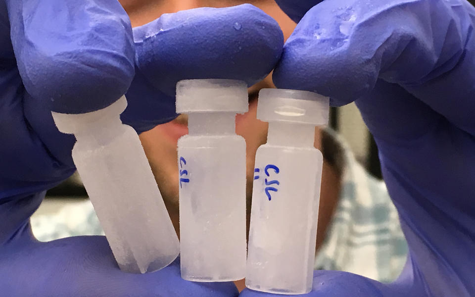 purple-gloved researcher holding three vials up to the camera