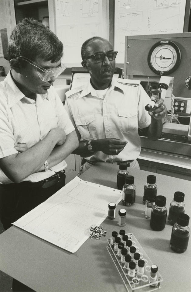 Two men in a lab with vials of oil in front of them.