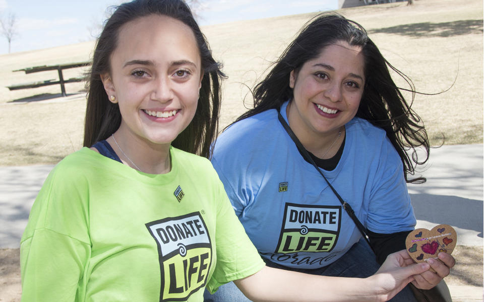 2018 Baldrige Award Recipient Donor Alliance photo showing two female volunteers outside holding a heart with Donate Life shirts.