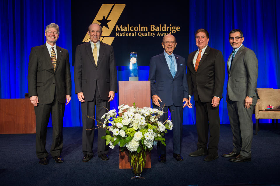 Middle: Baldrige Award on a podium. Left: two men in suits. Right: three men in suites