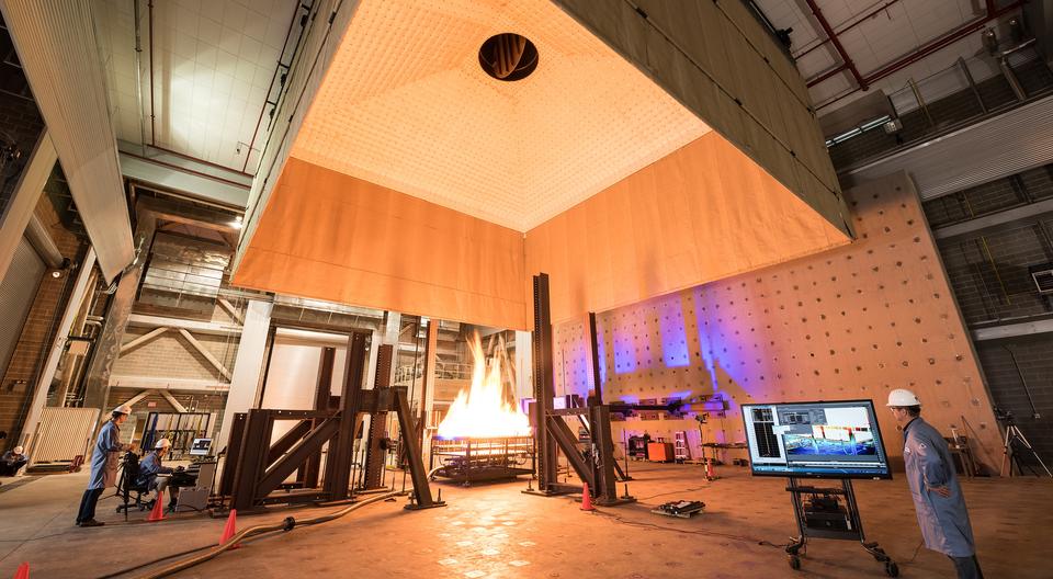 Photograph of large open room with fire engineers standing around a large fire test.