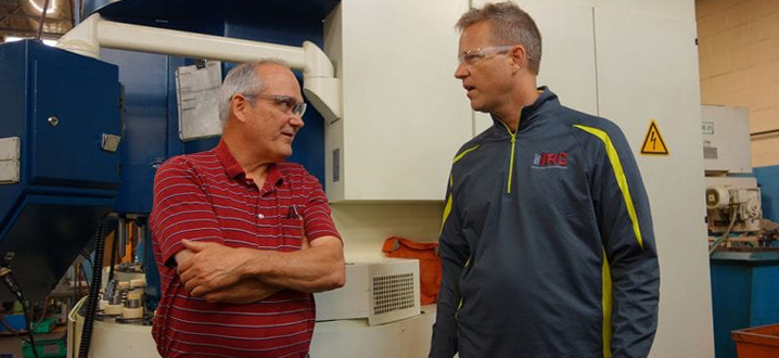 two men standing in a manufacturing factory talking about cobots