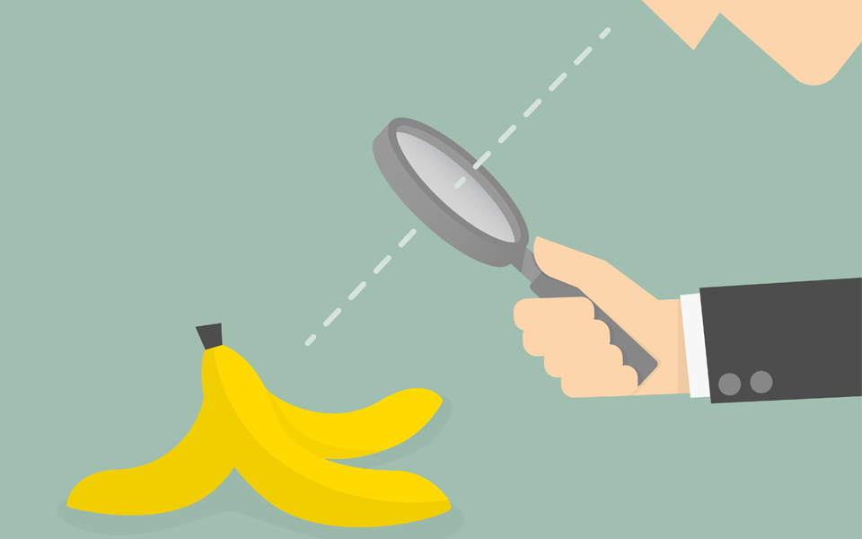 Image of a businessman looking a through a magnifying glass at a banana peel.