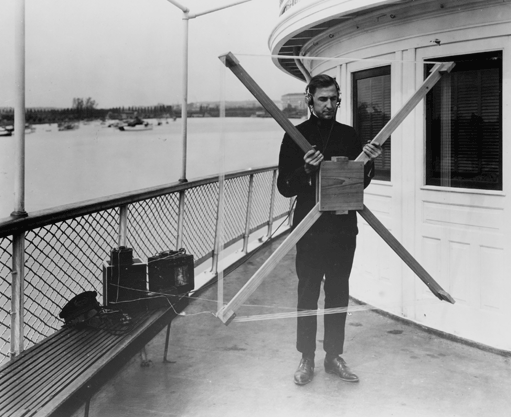 Man standing on a boat holding a radio direction finder, which looks like a kite without any fabric