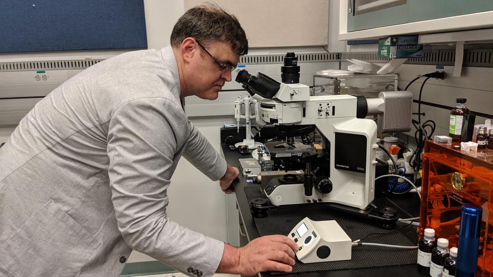 man adjusting a white colored optical microscope