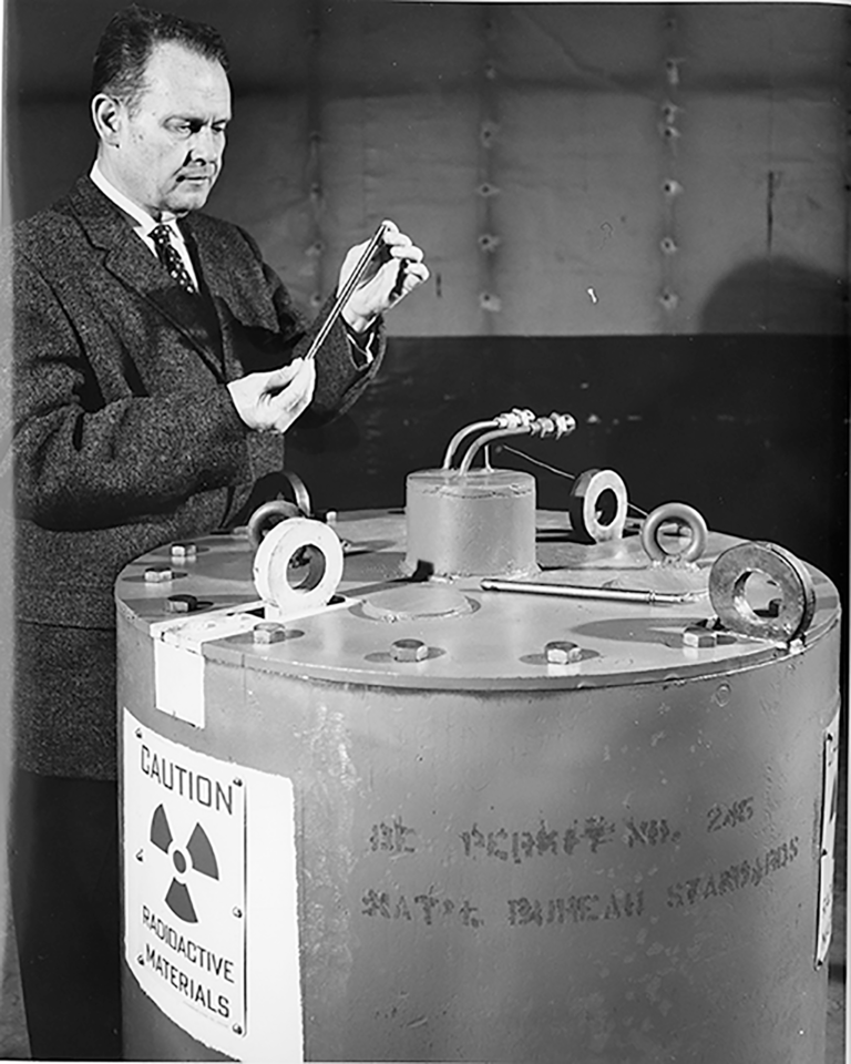 A man in a suit stands next to a large metal tank.