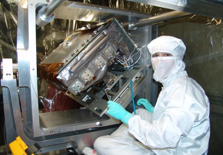 Person in a clean suit places a detector package in a scientific instrument