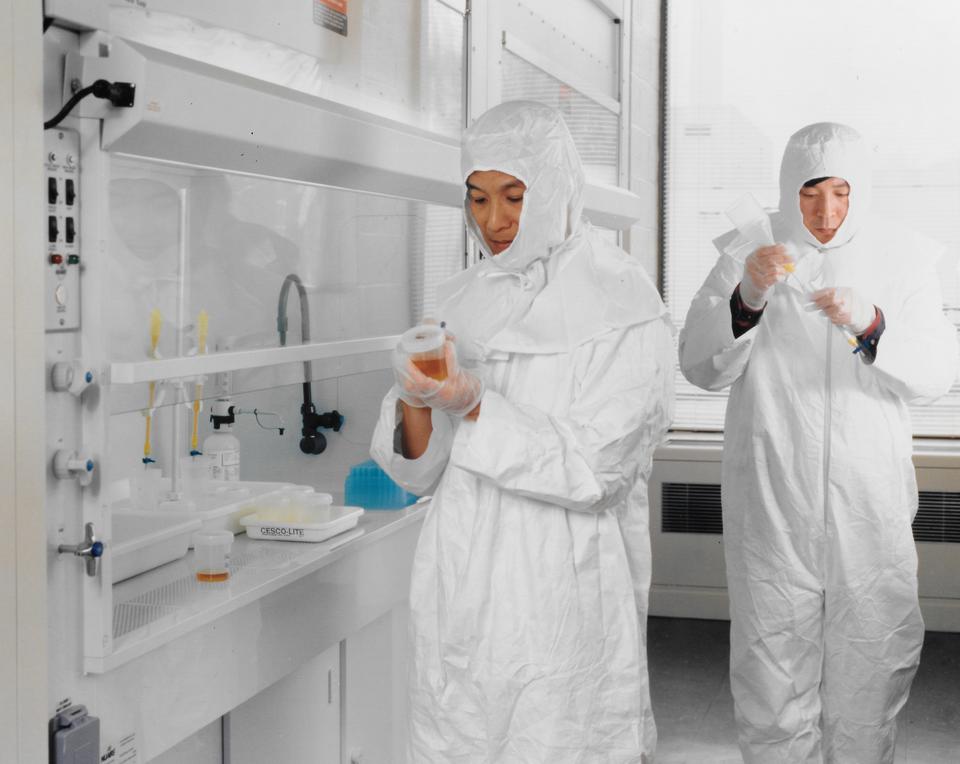 Two people in white coveralls work in a white lab