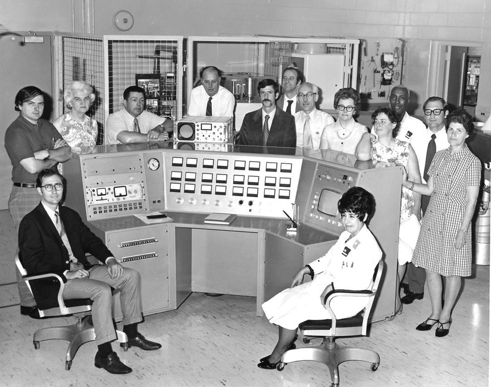 14 individuals sitting in front of scientific equipment