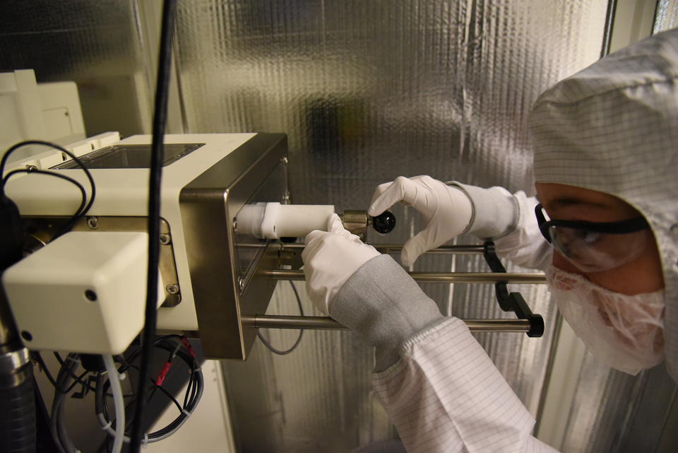 A woman in a clean suit loads a sample into a microscope