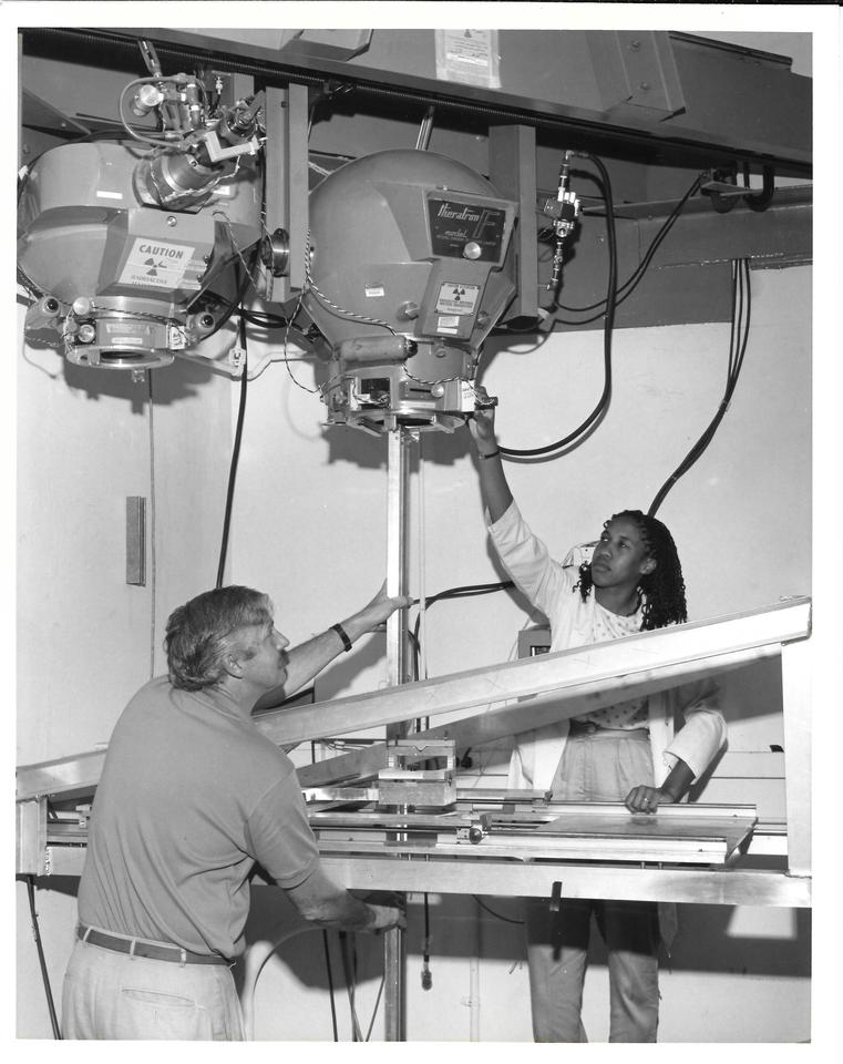 Two scientists on either side of a large machine with overhead components