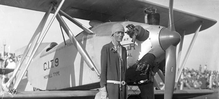 Black and white photo of Amelia Earhart standing in front of her plane