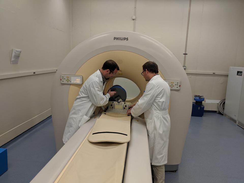 Two men in lab coats stand beside a large scanner