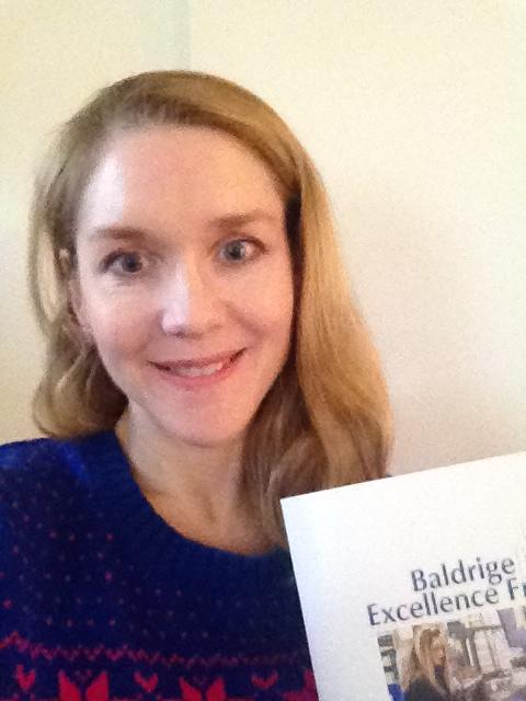 Christine wears a holiday sweater and holds a Baldrige framework booklet