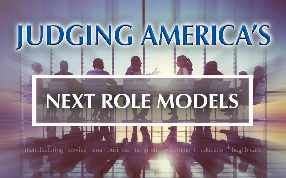 People at table judging America's next role model organizations in manufacturing, service, small business, nonprofit, government, education, and health care. 