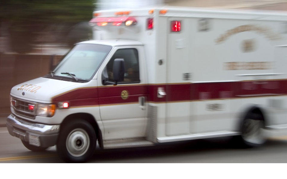 white ambulance with red trim and letters on side with lights flashing as it responds to a call