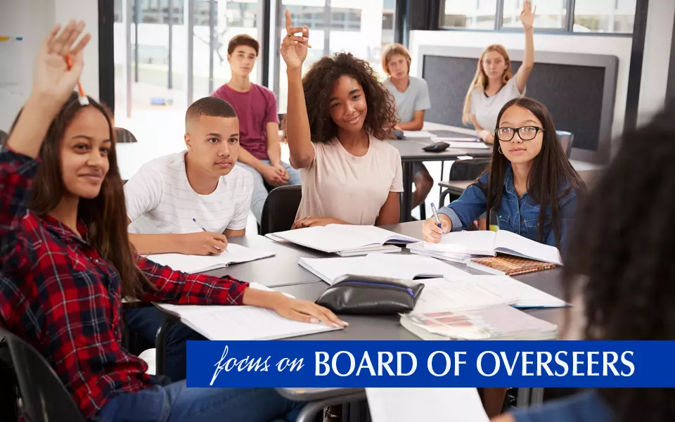 Focus on Overseers Pat Greco image of students raising their hands to answer teacher's question.