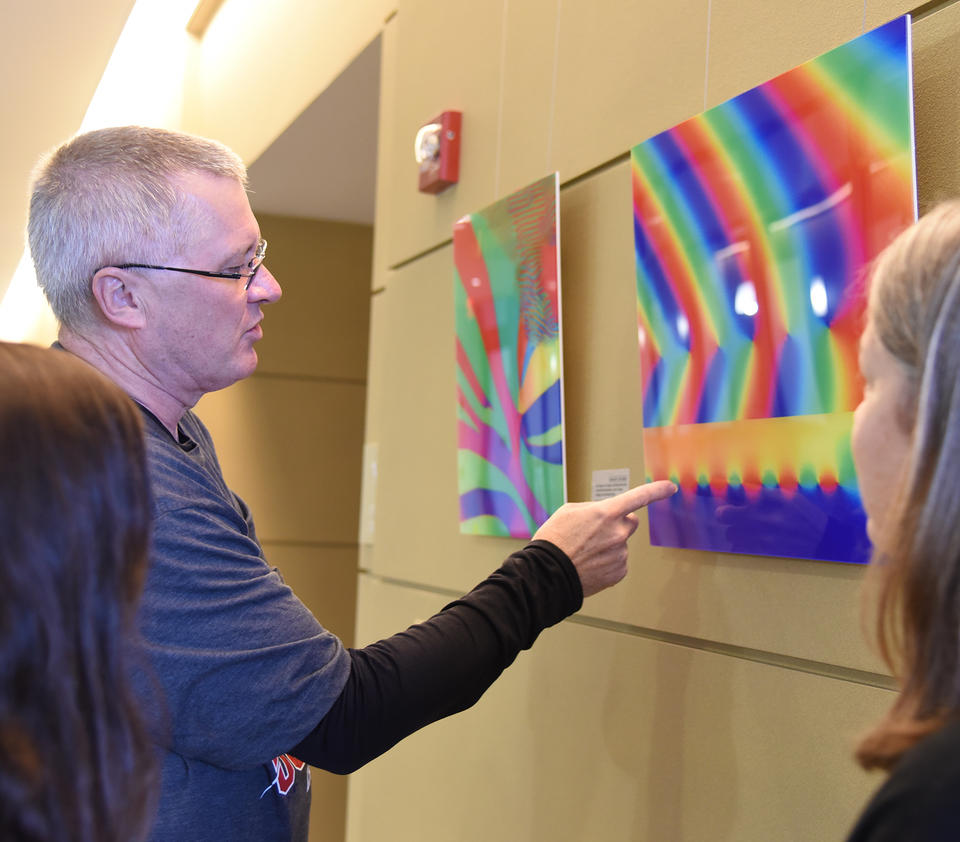 A man points out detail in a colorful image hanging in a gallery