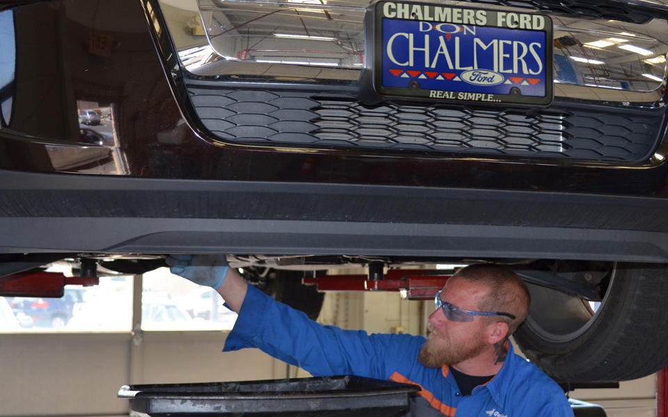 Don Chalmers Ford employee under vehicle changing the oil of a car.