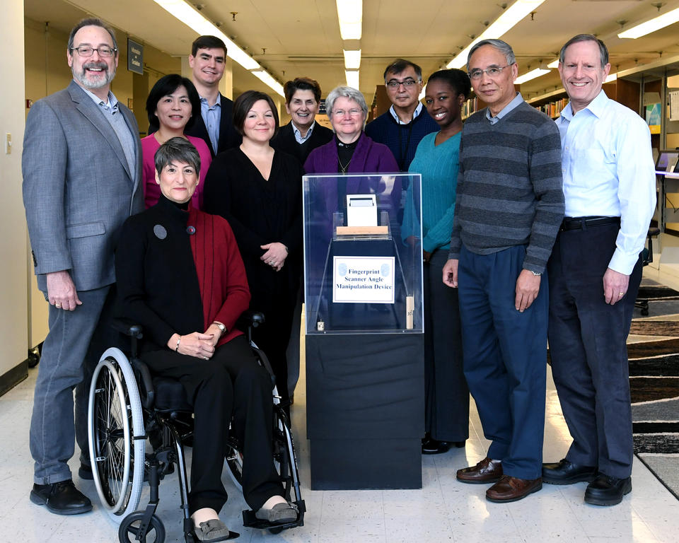 The NIST Biometrics Usability team poses next to the fingerprint scanner angle manipulation device