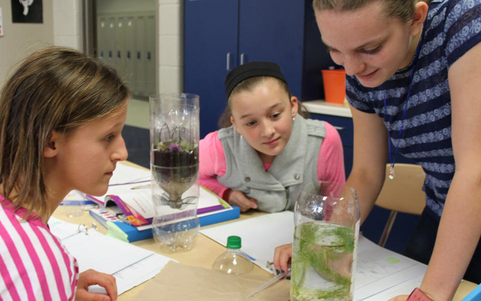 Pewaukee School District Measure What You Treasure blog photo showing three middle school female student doing a science experiment with a two liter plastic bottle.