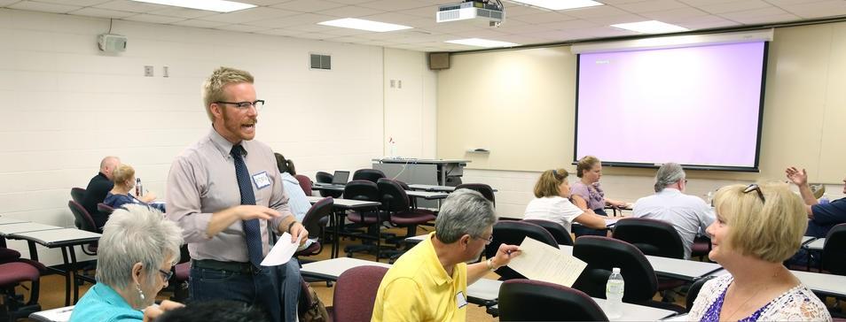 A male standing and other seated UW–Stout faculty and staff members are pictured in a classroom in an apparent discussion.