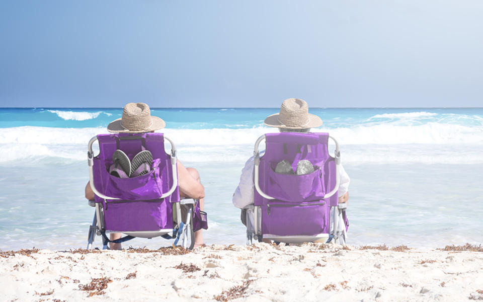 Two mature people sitting in chairs on the beach relaxing watching the ocean.