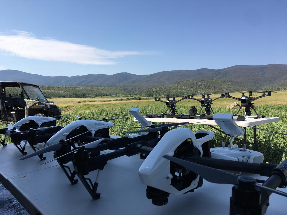 Seven drones lined up on the ground before takeoff. 
