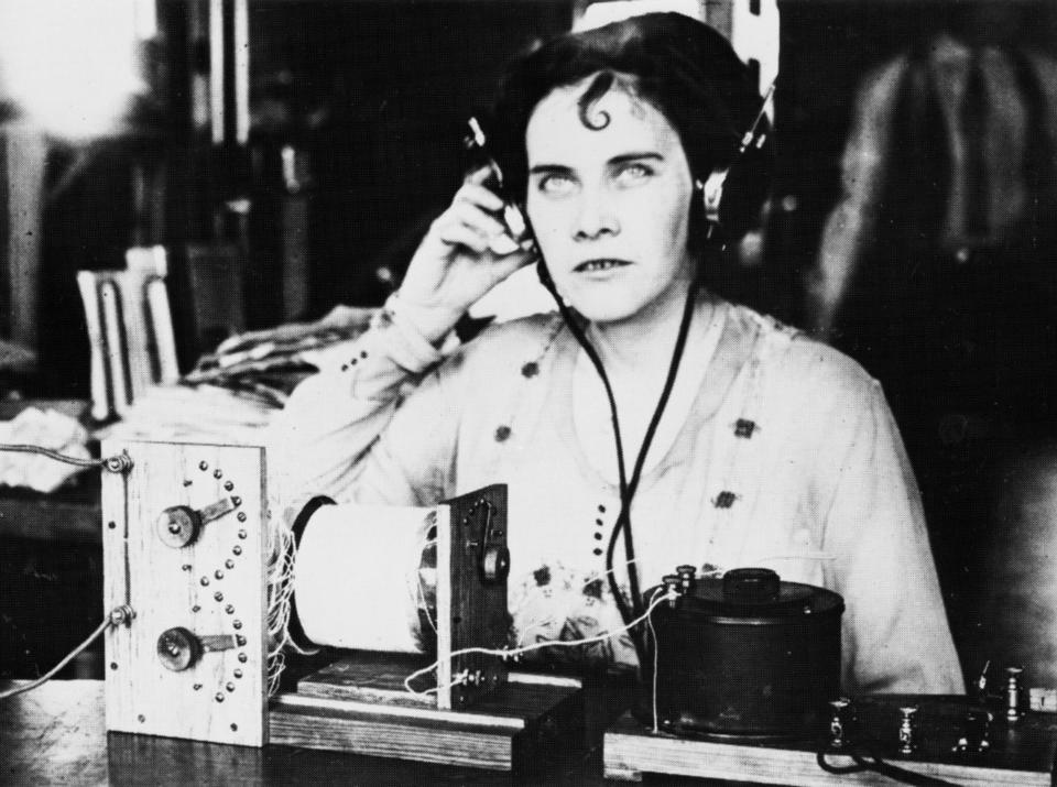 old photo of a woman with a headset on listening to an ancient-looking radio