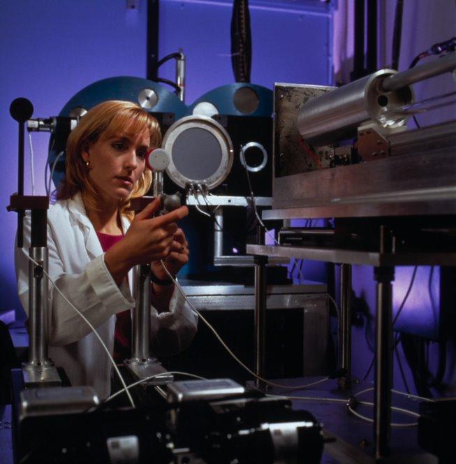 A woman in a lab coat adjusts a piece of scientific equipment