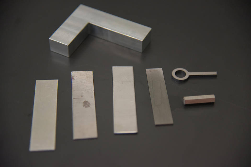 Several rectangular pieces of flat metal, a fake key and a rectangular "gun shaped" piece of metal are arranged on a table.