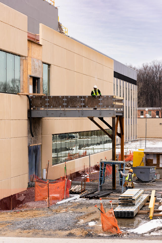 construction scaffolding attached to a building. A man stands on the scaffolding and a man stands below it.