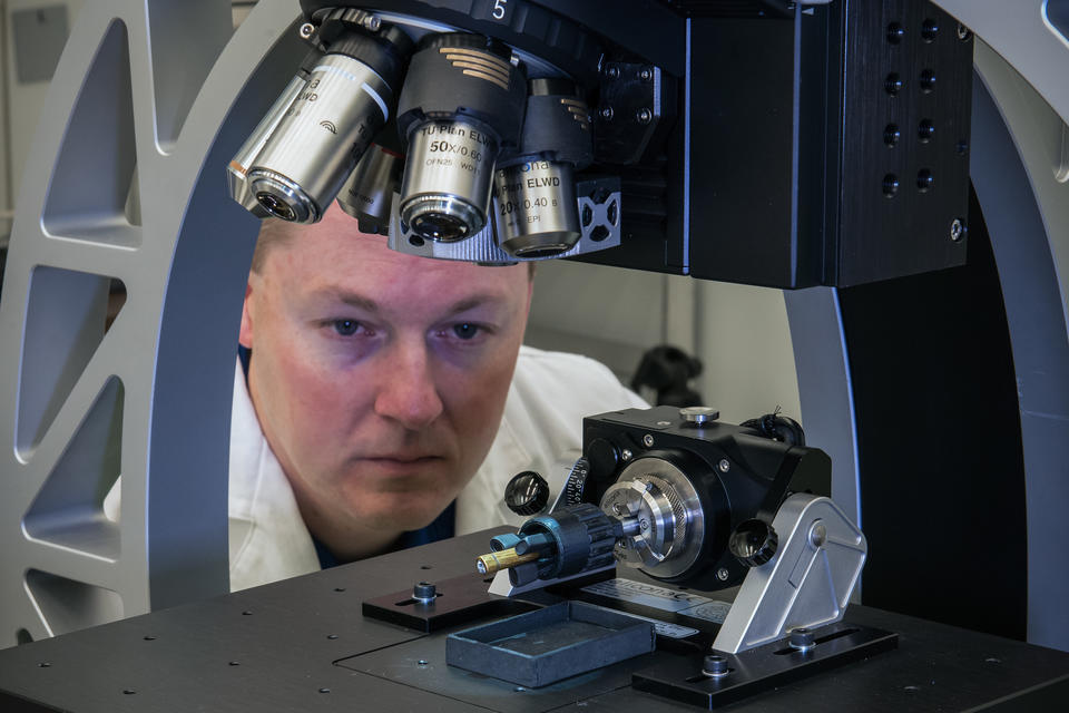 A man looks at the sample held under a microscope.