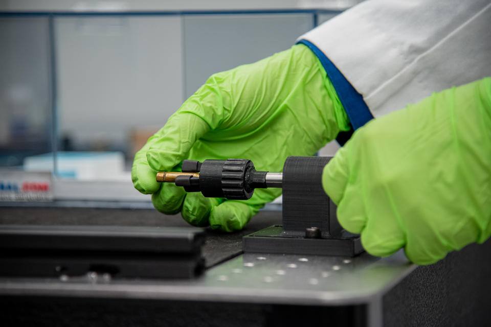 Person wearing green gloves positions bullet in holder.