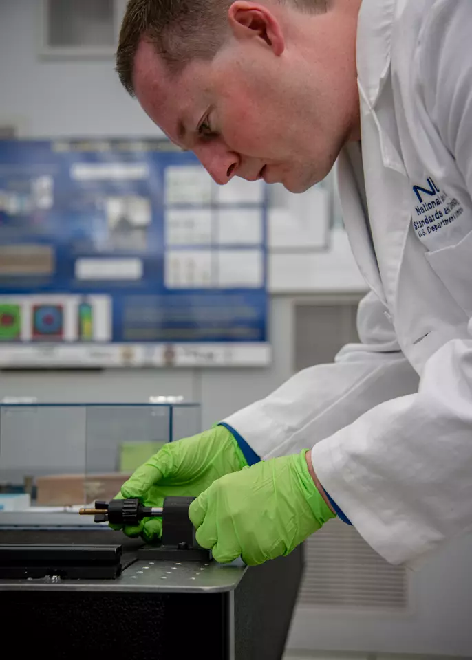 Man in lab coat leans over bullet in holder.