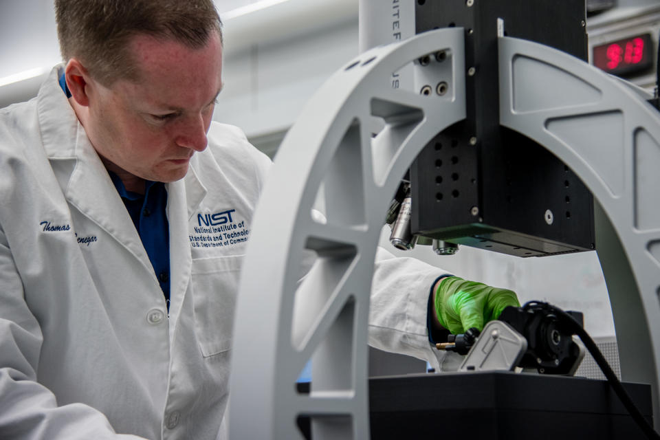 Man in lab coat reaches under microscope to place sample.