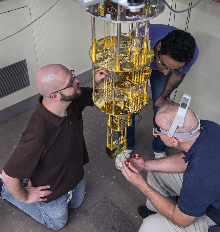 Three men work on a device that is hanging from the ceiling.