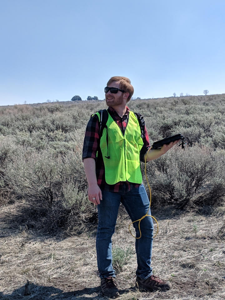 A man in a high-visibility vest (Jordan O'Dell) stands outside holding a black device.