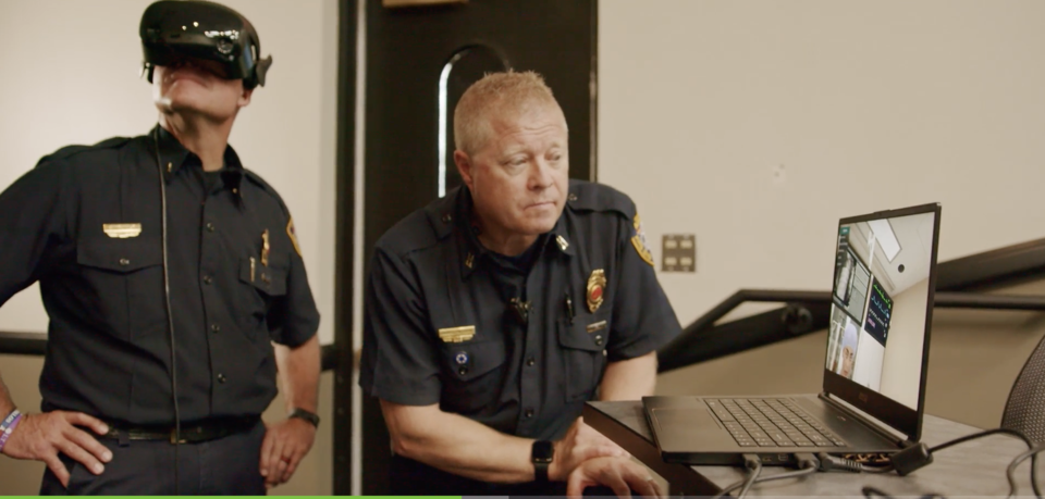 This image shows two first responders in uniform, one is observing a laptop and the other is wearing a VR headset.